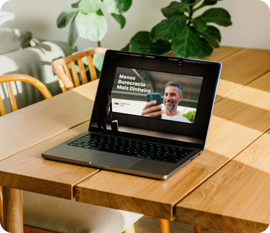 Laptop com tela exibindo homem sorrindo e texto "Menos Burocracia Mais Dinheiro